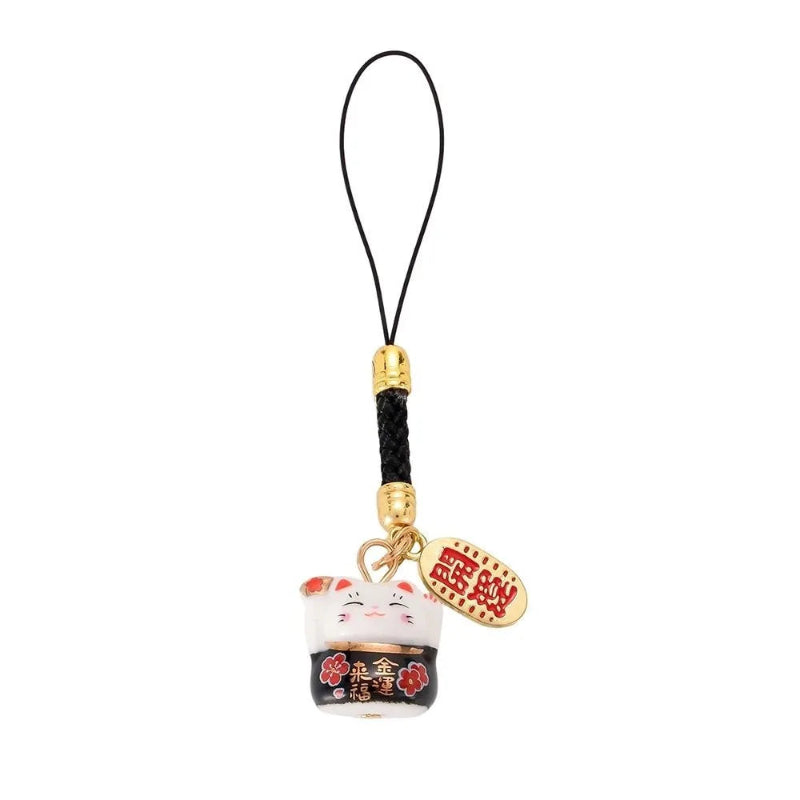 A Japanese lucky cat charm keychain featuring a white and black enameled lucky cat, a gold-plated bell, and a red and gold hanging tag with Japanese characters, attached to a black cord with gold spacer beads.
