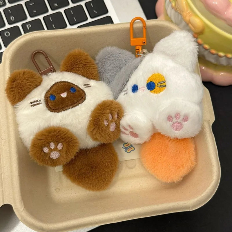 Two plush keychains, one brown and one white with orange, on a beige tray.
