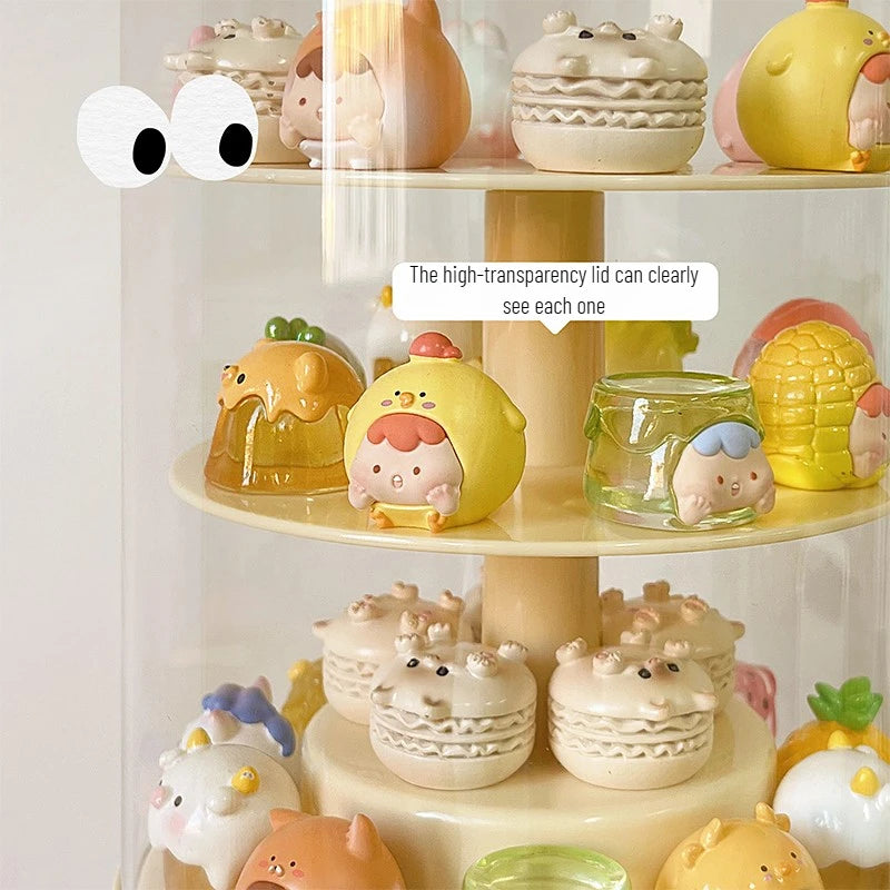 A tiered display stand filled with small pastel figurines and translucent decorative pieces, photographed indoors against a soft light background. A text bubble says the high-transparency lid can clearly see each one.