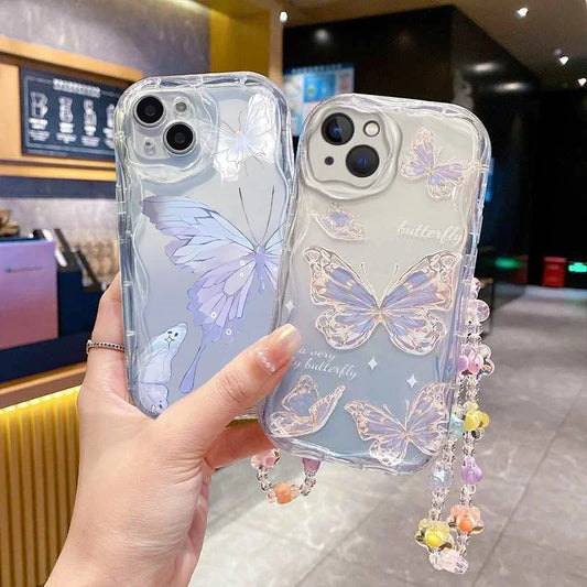 Clear phone cases with butterfly designs held by a hand in an indoor setting. One butterfly case has hints of blue into the case and butterfly design while the other just has it in the background and the butterfly is outlined with gold glitter