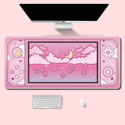 A pink desk mat with a cute cartoon sky design, shown under a computer monitor with a keyboard and mouse on a light pink background.