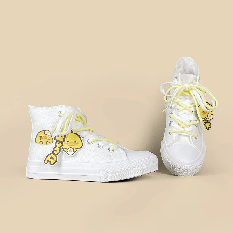 A pair of white high-top sneakers with pastel yellow laces and yellow cartoon duck charms, displayed on a solid beige background.