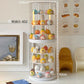 A tall cylindrical rotating display shelf with a clear acrylic outer cylinder and white inner tiers, shown in a styled room setting. The shelf holds many small pastel character figurines.
