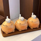 Three small ceramic kitchen containers with lid lids shaped like cartoon animals, arranged on a wooden tray against a kitchen background.