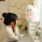 Woman sitting at a desk admiring a fluffy white pomeranian plush toy.