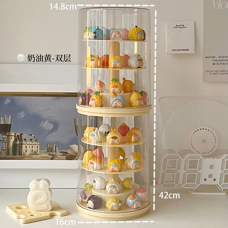 A clear cylindrical rotating display stand with multiple cream-colored shelves, filled with small pastel character figurines. White dashed measurement lines and text labels indicate dimensions: 14.
