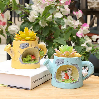 Two decorative planters shaped like a yellow watering can and a blue mug with animal designs on a wooden surface.