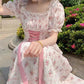 Woman in a floral dress with pink accents sitting outdoors.