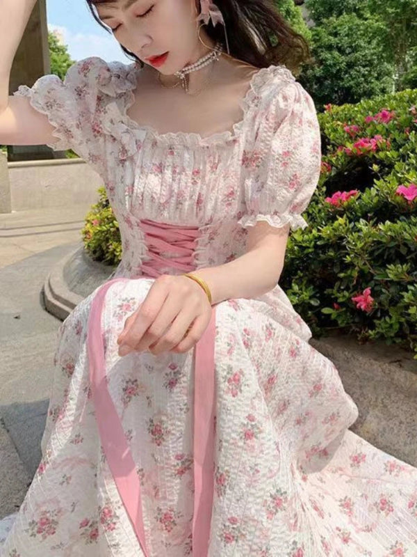 Woman in a floral dress with pink accents sitting outdoors.