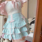 A close-up of a person wearing a light blue ruffled skirt with pink lace-up details and a white ruffled top in an indoor room setting.