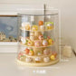 A 4-tier rotating acrylic display stand with a clear cylindrical dome cover and cream-colored base, shown on a tabletop with dimension labels overlaid (21.5 cm top, 25.