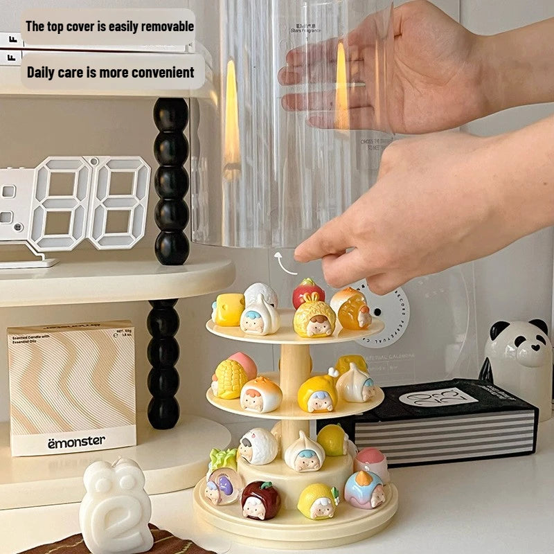 A three-tier rotating display stand holding small pastel character figurines, shown on a tabletop with a hand reaching toward it. The scene includes a digital clock, candle, books, and a panda figurine in a styled indoor setting.
