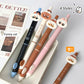 Four cute sassy cartoon cat-shaped pens in different colors on a surface with a magazine in the background.