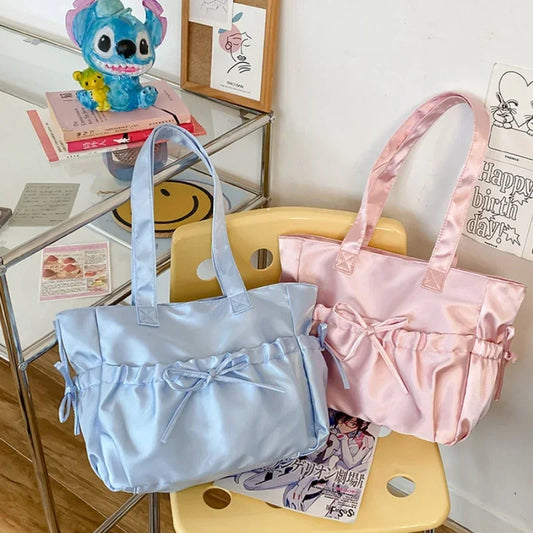 Two kawaii tote bags, one light blue and one pink, on a yellow chair with a shelf in the background.