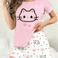 Person wearing a pink top with a kawaii cat face design and white shorts with cat print on a light background