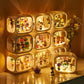 A set of nine illuminated display boxes arranged in a 3x3 grid on a tabletop, each lit from within to showcase small collectible figurines and toys. The boxes have rounded rectangular shapes with warm white lighting and are photographed in a cozy indoor setting with decorative flowers and a small figurine in the foreground.