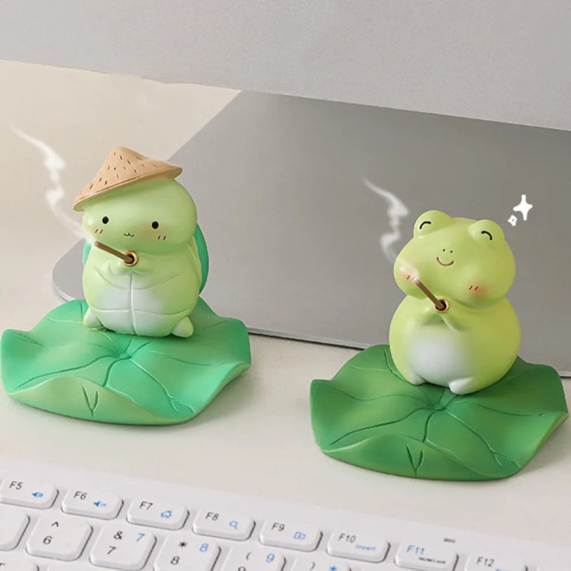Two kawaii  frog figurines on leaves in front of a laptop