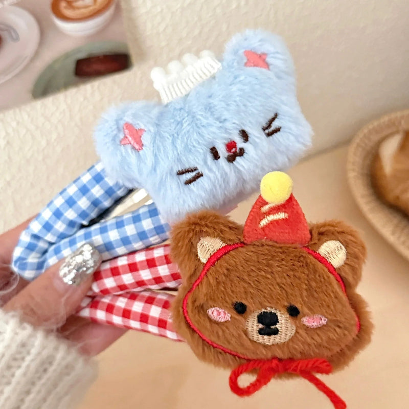 Two plush animal hair clips, one blue and one brown, held by a hand on a blurred background.