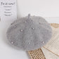 Gray beret with pearl embellishments on a textured surface with motivational text.