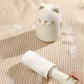 White cat-shaped roller with a hand holding it on a textured beige surface