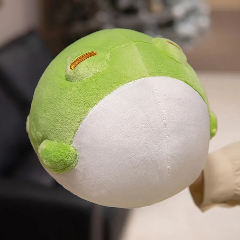 Hand holding Kawaii green and white frog plushie against a blurred background  