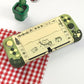 Green and beige phone case with cartoon designs on a white surface with a red checkered cloth.