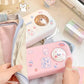 Two pink and white pouches with cartoon designs held by hands on a light background.