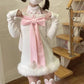 Person wearing a white outfit with a large pink bow in a room with wooden stairs.