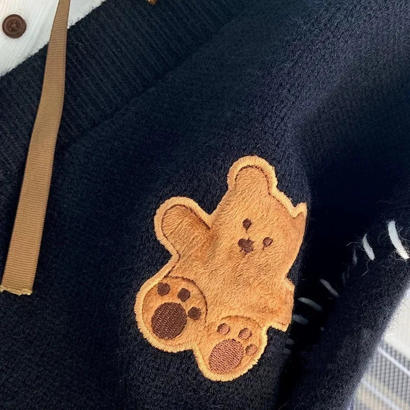 Sweet Teddy Bear Cardigan black edition with a bear sown into the chest area whilst the sleeves have large white stitches where they have been joined and black strips on the wrist cuffs with white, black and white trim, this image is showing a close up design of the bear sat and putting its arms out.