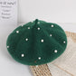 Green beret with pearl embellishments on a textured surface
