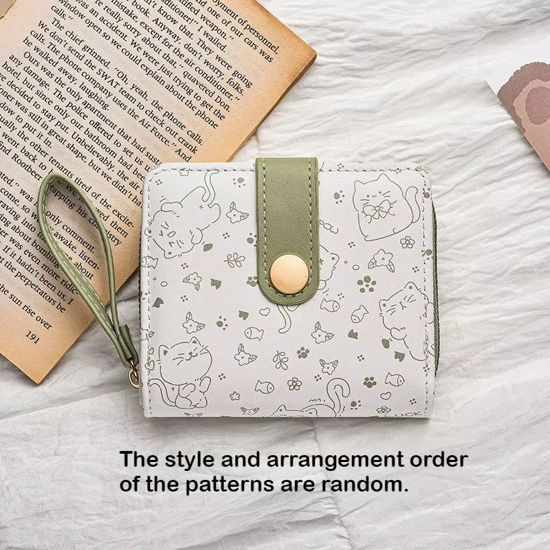 Small white wallet with cat pattern and green strap on a textured surface