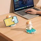 Two kawaii onsen cat phone holders on a wooden desk next to a person using a laptop computer