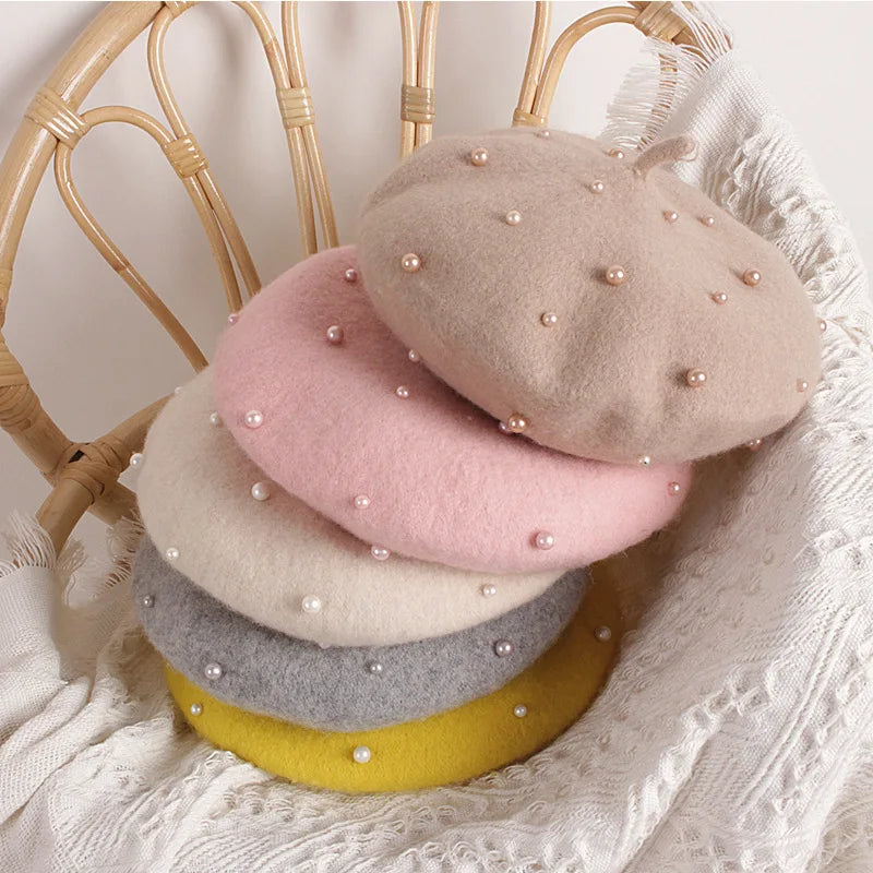 Stack of colorful berets with pearl embellishments on a textured surface.
