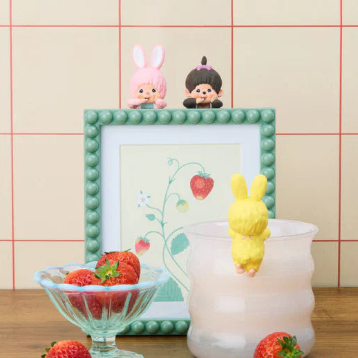 Decorative setup with small figurines, a candle, and a framed picture on a wooden surface.