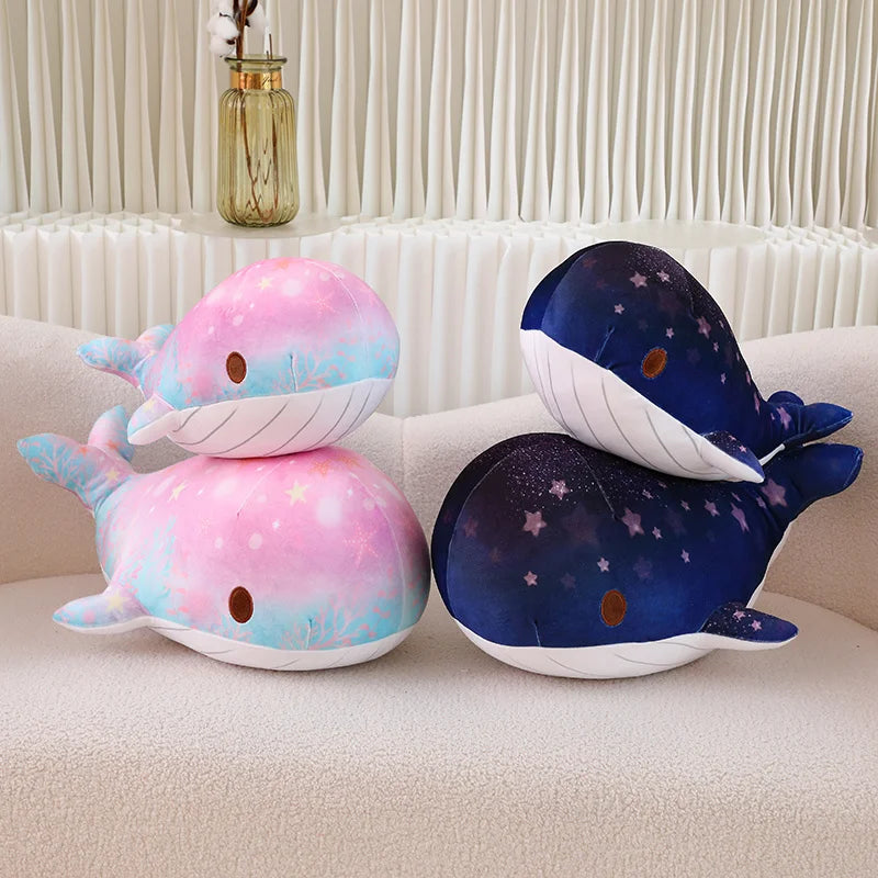 Two plush whale toys, one pink and one blue, on a beige couch.
