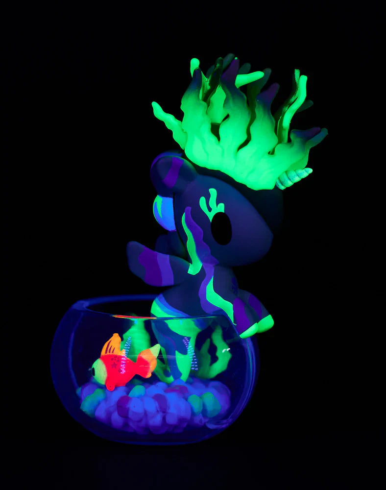 Glow in the dark unicorn figurine with fish and plants in a dark setting