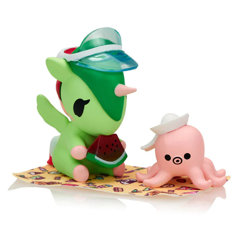 Two small figurines, a green unicorn-like character and a pink octopus, on a yellow towel with a white background.